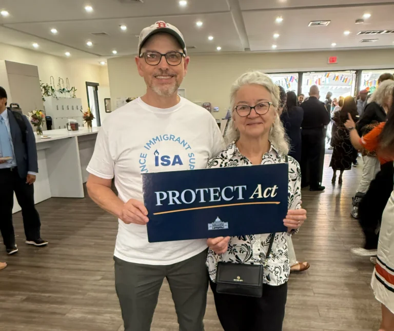 Two members of the Immigrant Support Alliance holding a sign that says "Protect Act"